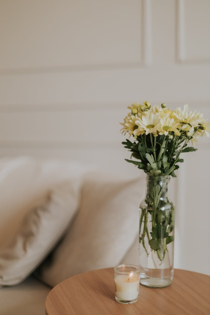 Elegant minimalist decor featuring flowers in a vase and a lit candle on a wooden table.