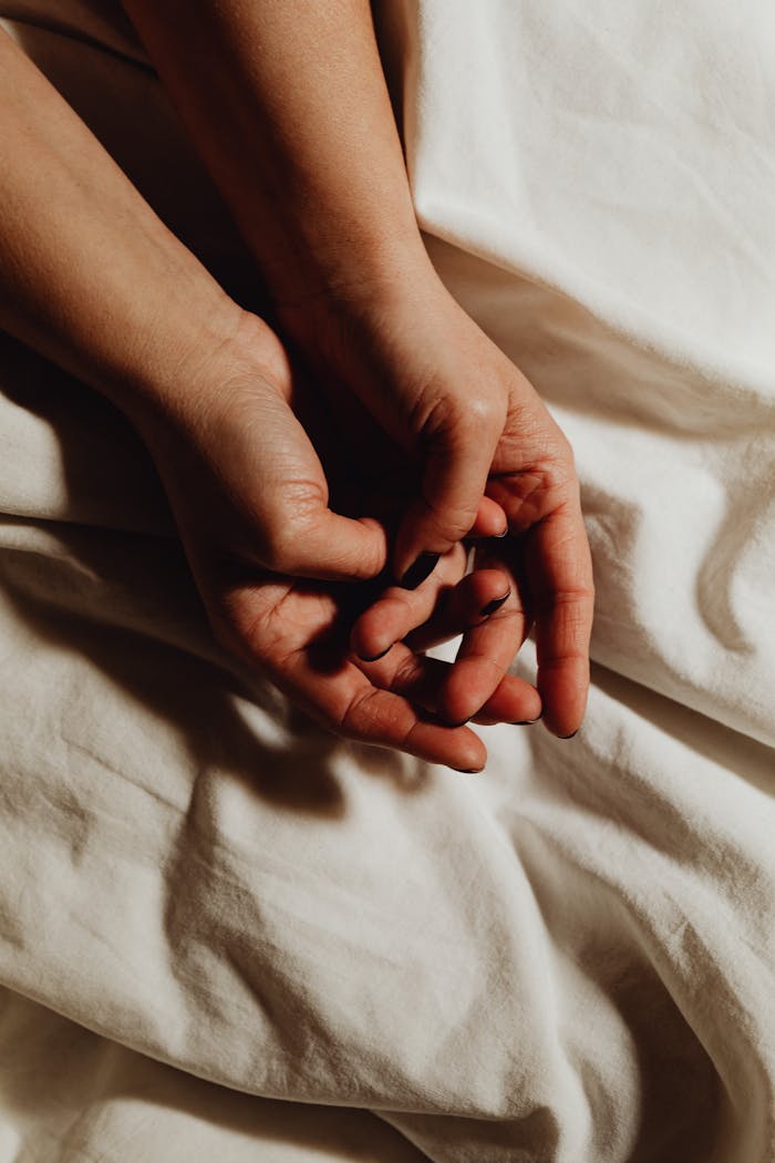 A close-up view of hands resting gently on soft white sheets, creating a peaceful and intimate scene.